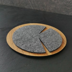 May include: A round wooden coaster with a gray felt insert divided into three sections. The coaster is perfect for protecting surfaces from heat and scratches.