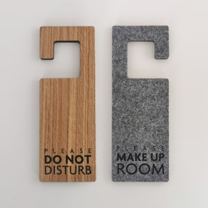 May include: Two wooden door hangers with a cutout for hanging on a door knob. The left hanger is wood with the text "PLEASE DO NOT DISTURB". The right hanger is gray felt with the text "PLEASE MAKE UP ROOM".