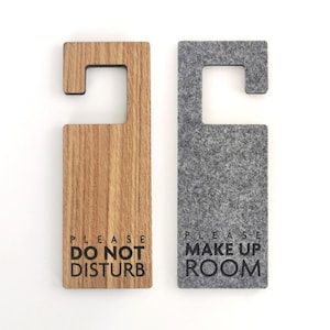 May include: Two rectangular door hangers with a hook at the top. The left hanger is light brown wood with the black text PLEASE DO NOT DISTURB. The right hanger is dark gray felt with the black text PLEASE MAKE UP ROOM printed on the front.