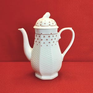 May include: White ceramic coffee pot with a red and white floral pattern. The pot has a lid and a handle.
