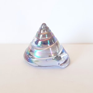 May include: A iridescent glass seashell sculpture with a spiral design. The shell is a light blue color with a pearlescent finish.