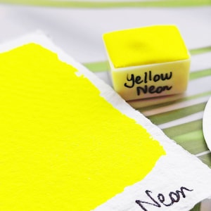 Puede incluir: Una muestra de pintura acuarela amarilla neón con el texto "Yellow Neon" escrito en ella.