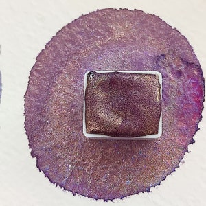 Könnte beinhalten: Nahaufnahme einer violetten Aquarellfarbe mit schimmerndem Finish. Die Farbe befindet sich in einer weißen Plastikwanne mit einem durchsichtigen Deckel.