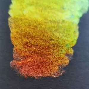 May include: A close-up of a shimmery, iridescent paint sample. The paint is a gradient of yellow, orange, and red, with a hint of green at the top. The paint is thick and textured, and it appears to be wet.