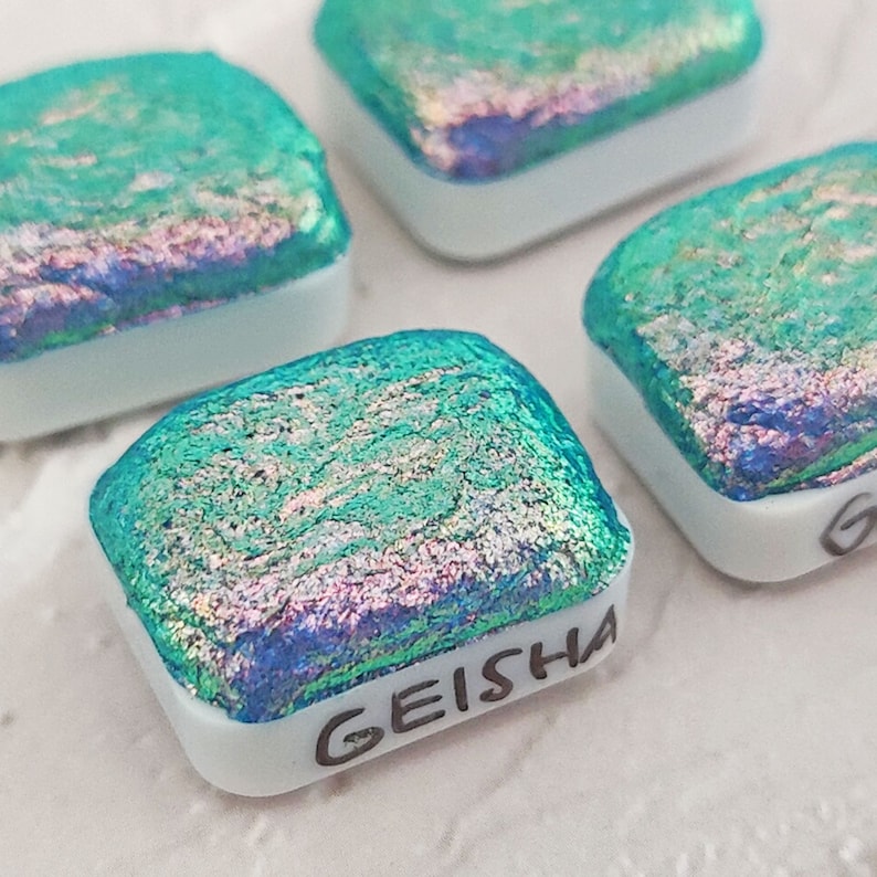 May include: Four square iridescent glass tiles with a white backing. The tile in the foreground is labeled "GEISHA".