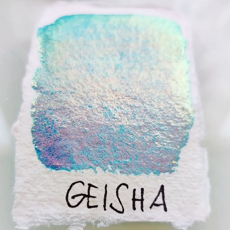 May include: A close-up of a light blue iridescent ink sample with the word "GEISHA" written in black ink below.