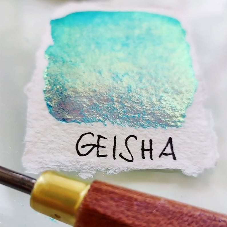 May include: A swatch of iridescent teal watercolor paint with a light green gradient. The paint is labeled "GEISHA" in black ink.