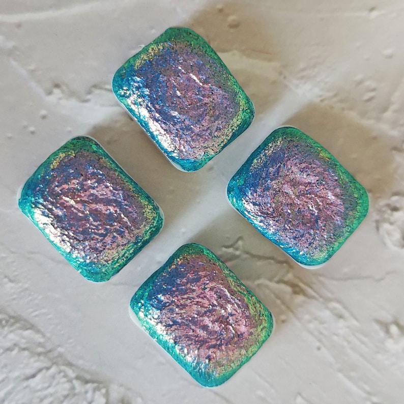 May include: Four iridescent glass tiles in a square shape with a teal blue and pink color scheme.