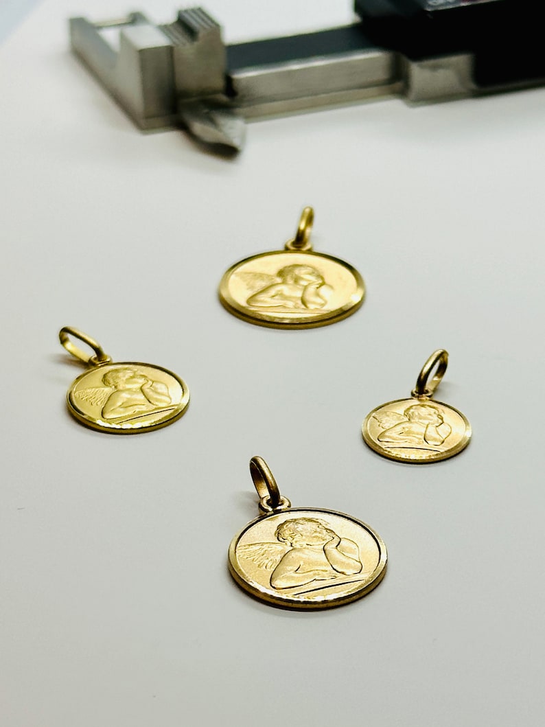 May include: Four gold angel pendant charms of varying sizes. Each charm features a detailed depiction of an angel with wings and a cherubic face.