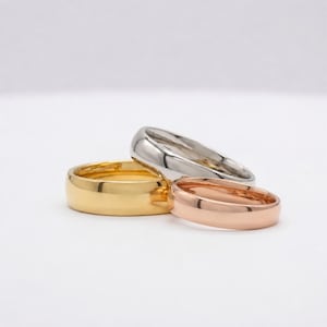 Peut inclure: Un ensemble de trois bagues en métal lisse et poli empilées ensemble. La collection comprend une bague en or jaune, une bague argentée et une bague en or rose. Chaque anneau présente un profil arrondi simple avec une finition brillante.