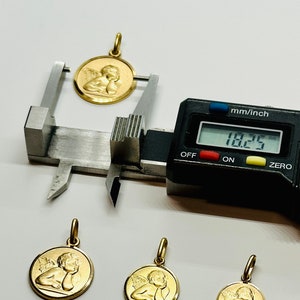 May include: Four gold angel pendants of varying sizes. The largest pendant is being measured with a digital caliper, which reads 18.25 mm.