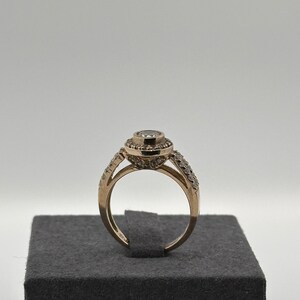 May include: A gold ring with a large, clear, round gemstone surrounded by smaller gemstones. The ring is on a gray velvet ring box.