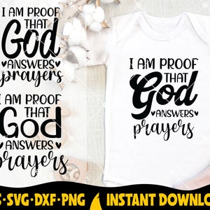 May include: A white onesie with black text that reads "I am proof that God answers prayers". The onesie is on a white background with cotton balls.