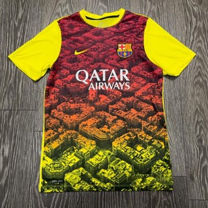 May include: A short-sleeved football shirt featuring bright yellow sleeves and a central panel with a gradient print of a city grid transitioning from dark red to yellow. The shirt displays the FC Barcelona crest, a yellow Nike swoosh, and the text QATAR AIRWAYS.