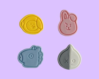 May include: Four colorful silicone cookie cutters shaped like cartoon characters. The cutters are yellow, pink, blue, and gray and white.