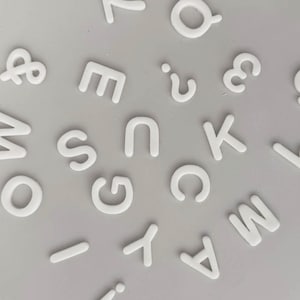 May include: White plastic letters of the alphabet and punctuation marks on a gray background.