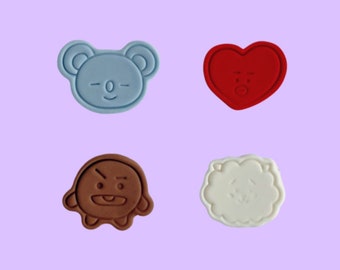 May include: Four silicone cookie cutters shaped like cartoon characters. The cutters are blue, red, brown, and white. The characters have different facial expressions.