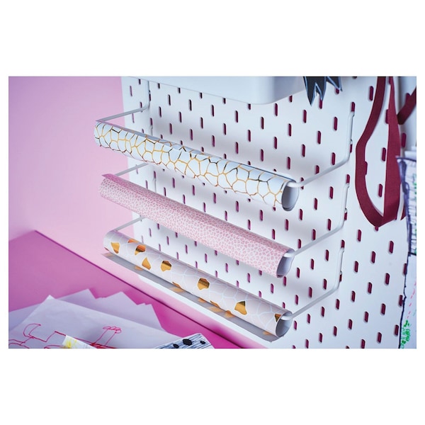 May include: White pegboard with a white metal rack holding four rolls of wrapping paper. The wrapping paper is patterned with gold and pink designs.