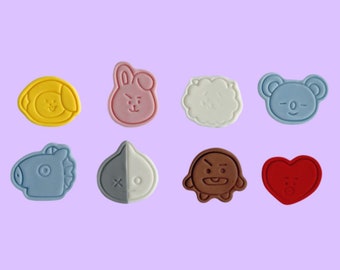 May include: Set of eight silicone cookie cutters featuring characters from the popular K-pop group BTS. The cutters are in various colors, including yellow, pink, white, blue, gray, and brown. Each cutter features a different character with a unique expression.