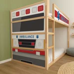 May include: A wooden bunk bed designed to resemble an ambulance. The bed features a white, red, gray, and black front panel with the word "AMBULANCE" and a star symbol. The top bunk has a similar design with the word "AMBULANCE".