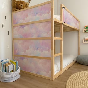 May include: A wooden bunk bed with a pastel cloud design on the headboard and side panels. The bed has a natural wood frame and a white mattress. A basket of books sits on the floor near the bed.