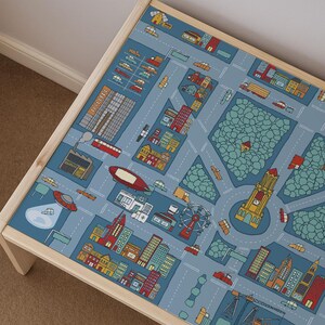 Peut inclure: Une table en bois avec une surface bleue imprimée d'une illustration détaillée de plan de ville. Le graphique comprend des routes, des bâtiments, une tour d'horloge, une grande roue, un dirigeable rouge, une soucoupe volante et divers véhicules.