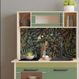 May include: A wooden toy kitchen playset with a green and black floral patterned backsplash, a black stovetop, a green sink, and two green cabinets with black handles.