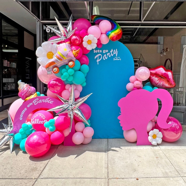 May include: A vibrant party display featuring a large blue backdrop with the words "lets go Party". The display includes pink, white, and teal balloons, a roller skate balloon, and a Barbie silhouette. The words "come on Barbie" are also visible.