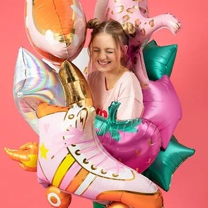 May include: A collection of colorful foil balloons, including a pink roller skate, a pink leopard, a strawberry, and star-shaped balloons. The balloons are in shades of pink, orange, green, and gold, creating a festive and playful atmosphere.