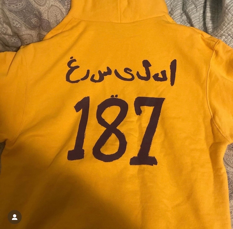 May include: Yellow hoodie with a purple Arabic phrase and the number 187 printed on the back.