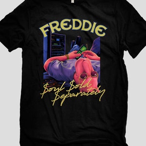 May include: Black t-shirt with a graphic of a pink figure laying down with a phone and sunglasses. The text "FREDDIE Soul Sold Separately" is printed in yellow on the shirt.