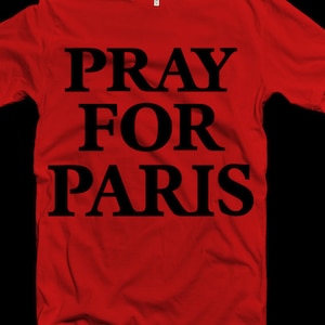 Może przedstawiać: Czerwona koszulka z napisem "Pray for Paris" w kolorze czarnym.