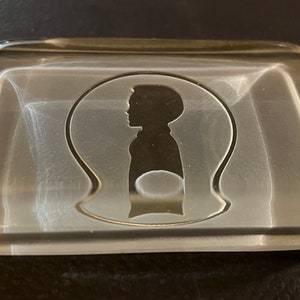 以下が含まれることがあります： ガラス製のペーパーウェイト。透明なガラスに人の頭と肩のシルエットがエッチングされている。