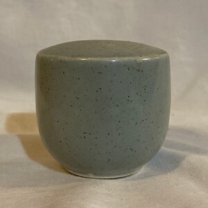 May include: A small, round, gray ceramic jar with a speckled glaze.