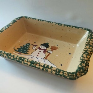 May include: A green and beige ceramic baking dish with a snowman and a Christmas tree design. The dish has a speckled glaze.