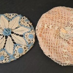 May include: Two crocheted doilies, one with a blue and white floral design and the other with a white and pink design.