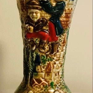 May include: A ceramic stein with a brown, white, and blue glaze. The stein features a raised design of two figures in medieval garb, a castle, and a coat of arms with a red lion.