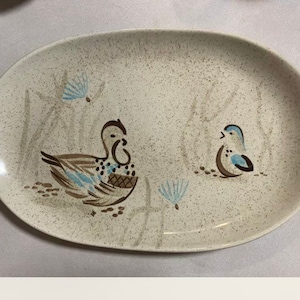 Puede incluir: Una fuente ovalada blanca con un esmalte moteado. La fuente presenta un diseño de pájaro marrón y azul con un diseño de pato marrón y azul.