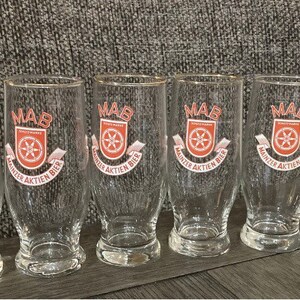 Peut inclure: Six verres à bière en verre transparent avec un logo rouge et blanc qui dit "MAB Mainzer Aktien Bier".