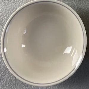 Könnte beinhalten: Eine weiße Keramikschüssel mit einem hellgrauen Rand. Die Schüssel ist rund und hat eine glatte, glänzende Oberfläche.