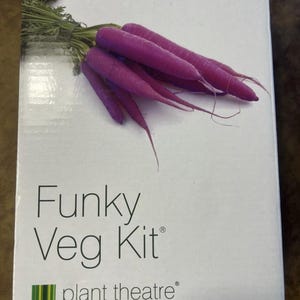 以下が含まれることがあります： 紫色のニンジンと緑色の葉の束が描かれた白い箱。「Funky Veg Kit」の文字が黒で印刷され、下に「plant theatre」のロゴがあります。