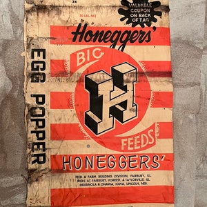 May include: A vintage brown paper bag with red and white stripes. The bag is labeled "Honeggers' Big H Feeds" and "Egg Popper". The bag is for 50 pounds of feed.