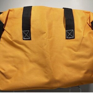 May include: A yellow duffel bag with black accents on the sides. The bag has two black handles with white stitching. The bag is made of a durable material, suitable for travel or carrying gear.