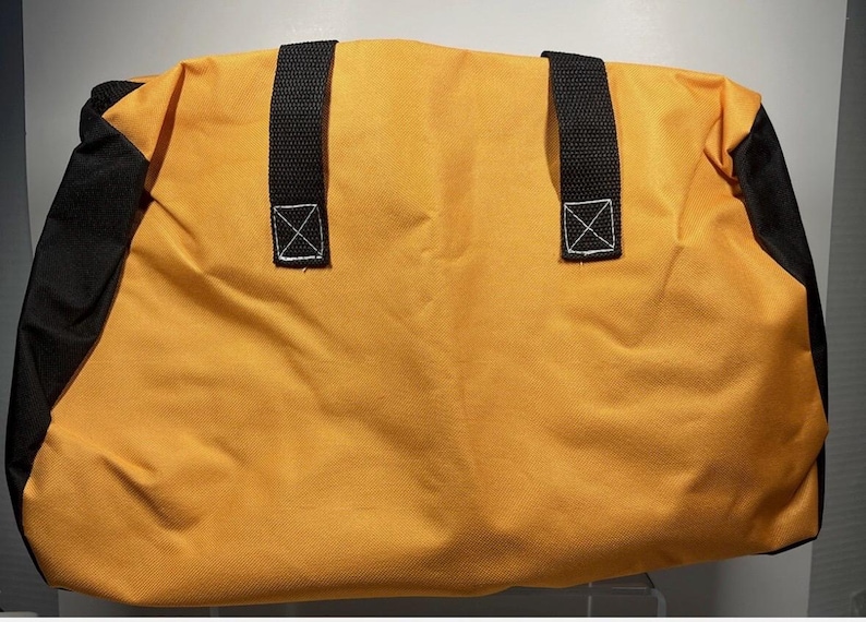 May include: A yellow duffel bag with black accents on the sides. The bag has two black handles with white stitching. The bag is made of a durable material, suitable for travel or carrying gear.