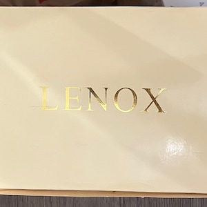 Peut inclure: Une boîte blanche avec le mot "LENOX" imprimé en lettres dorées.