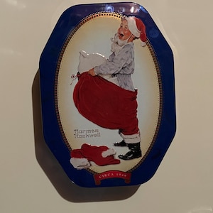 Könnte beinhalten: Eine blaue und goldene Dose mit einer Vintage-Illustration von Weihnachtsmann, der einen roten Sack trägt. Die Illustration stammt von Norman Rockwell und ist datiert auf circa 1949.