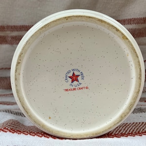 Puede incluir: La parte inferior de una taza de cer&aacute;mica blanca con un dise&ntilde;o de estrella roja, blanca y azul. El texto "Crafted with Pride in USA" y "Treasure Craft &copy;" est&aacute; impreso en la taza.