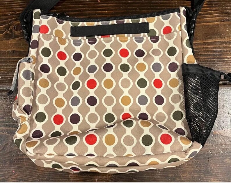 Puede incluir: Bolso de hombro beige con un patr&oacute;n repetitivo de c&iacute;rculos conectados en rojo, marr&oacute;n, gris y amarillo. El bolso tiene una correa negra, un bolsillo lateral de malla y un peque&ntilde;o bolsillo lateral.
