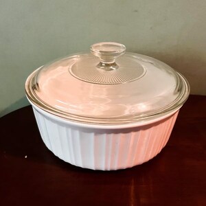 Puede incluir: Plato para hornear de cerámica blanca con tapa de vidrio. El plato tiene un diseño acanalado y la tapa tiene un pomo en la parte superior.