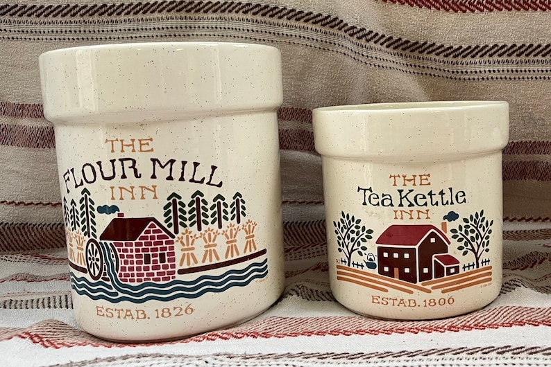 Puede incluir: Dos botes de cer&aacute;mica con un tema de casa de campo. El bote m&aacute;s grande es blanco con motas marrones y dice "The Flour Mill Inn Est. 1826". El bote m&aacute;s peque&ntilde;o es blanco con motas marrones y dice "The Tea Kettle Inn Est. 1800".